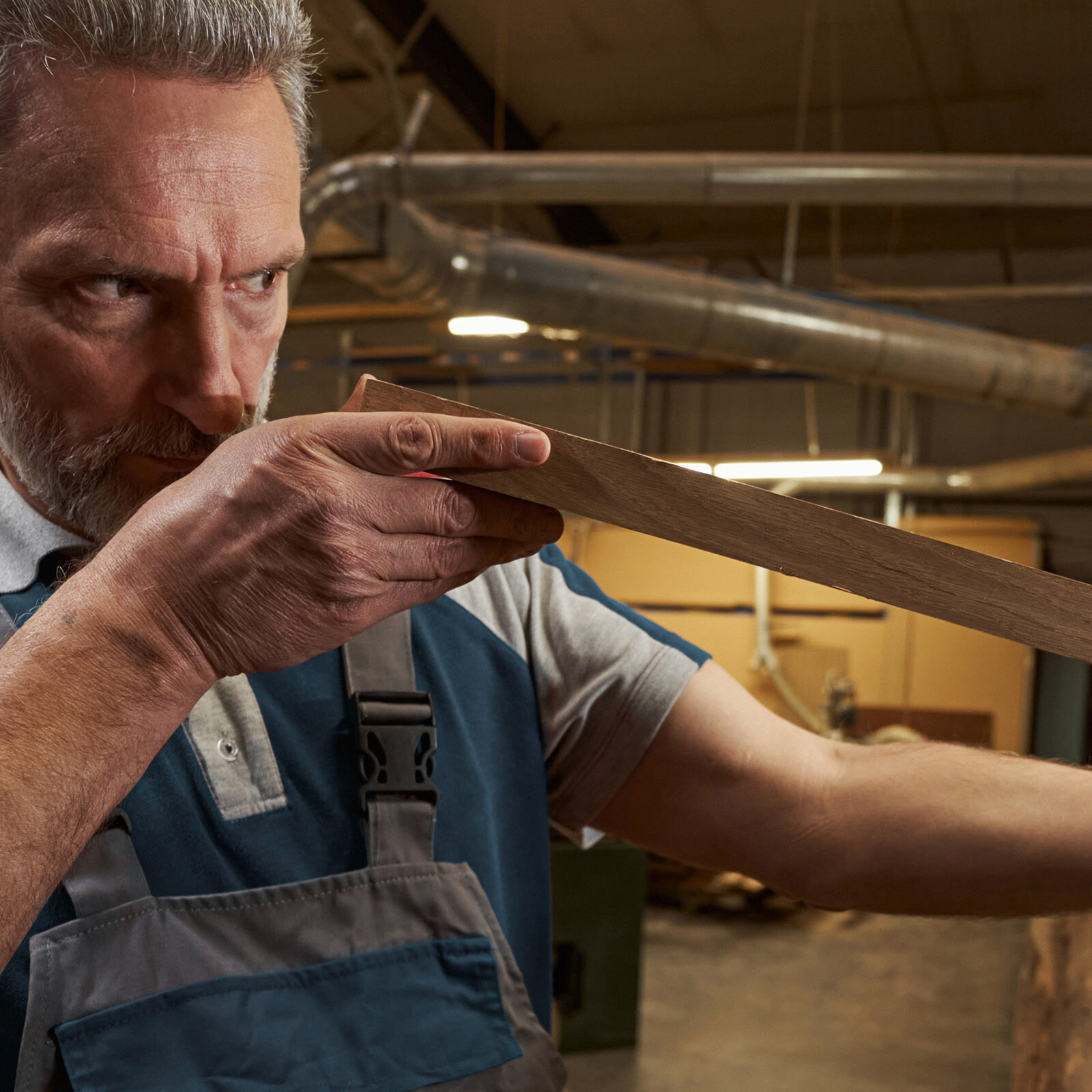 Serious carpenter holding wooden bar while standing near shelves